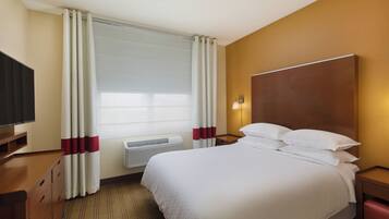 A hotel room with a large bed, a flat-screen TV, a heater, and a window with curtains.