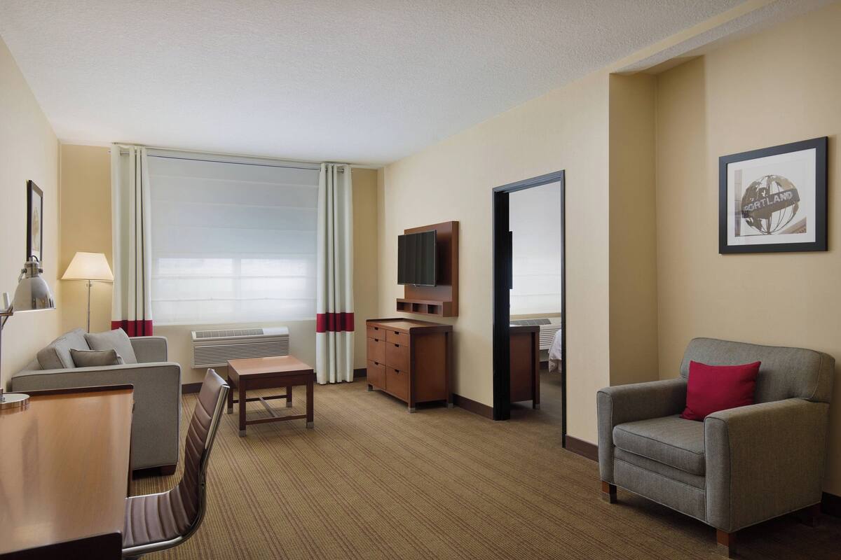 A hotel room with a sofa, armchair, TV, and a desk.