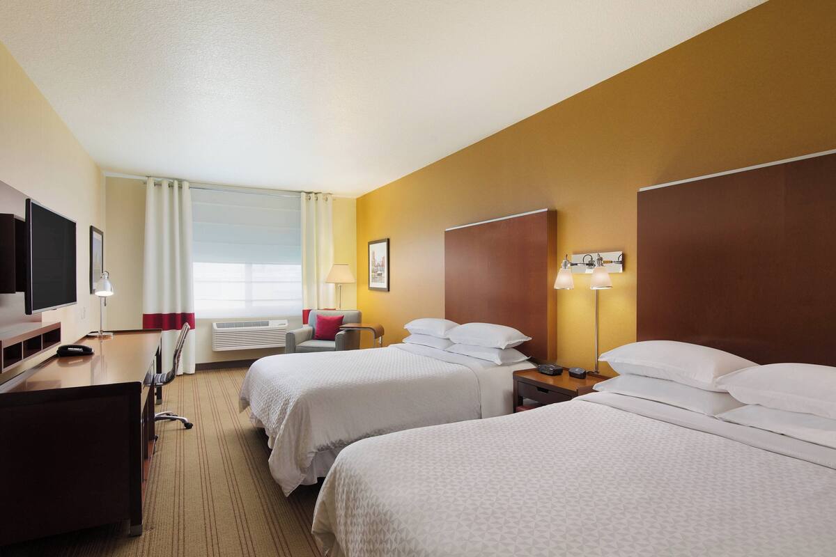 A hotel room with two beds, a desk, a TV, and a window with curtains.