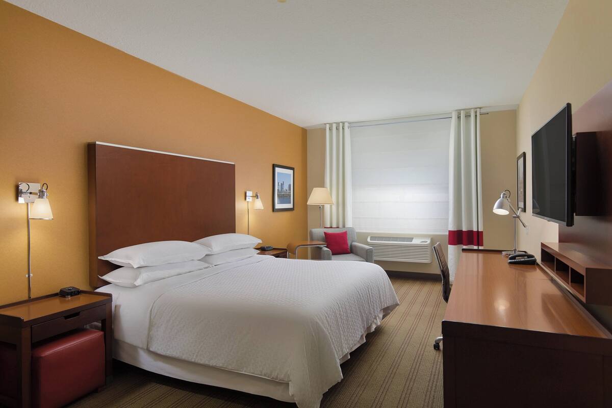 A hotel room with a large bed, a desk, a television, and a window with curtains.