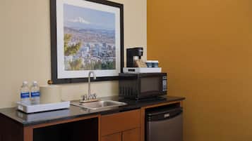 A small kitchenette with a sink, microwave, coffee maker, and water bottles.