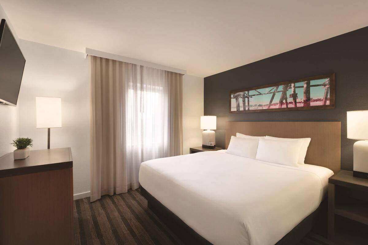 Ein Hotelzimmer mit einem großen Bett, zwei Nachttischen mit Lampen, einem Flachbildfernseher und einem Bild an der Wand.