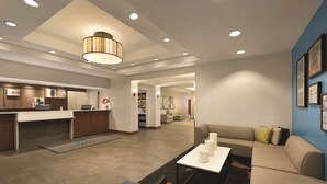 En modern hotellobby med en receptionsdisk, en sittgrupp och ett kök i bakgrunden.