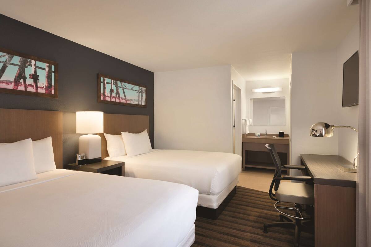 Ein Hotelzimmer mit zwei Betten, einem Schreibtisch, einem Stuhl, einer Schreibtischlampe und Bildern an den Wänden.