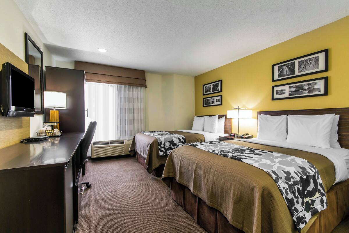 A hotel room with two beds, a desk with a TV, a lamp, and framed pictures on the wall.
