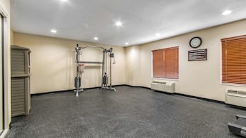Un gimnasio amplio con una barra de dominadas, un reloj y un cartel con las normas de seguridad en la pared.