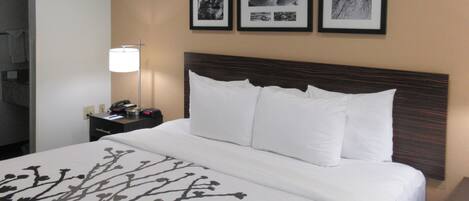 A hotel room with a large bed, a nightstand, a lamp, and three framed pictures on the wall.