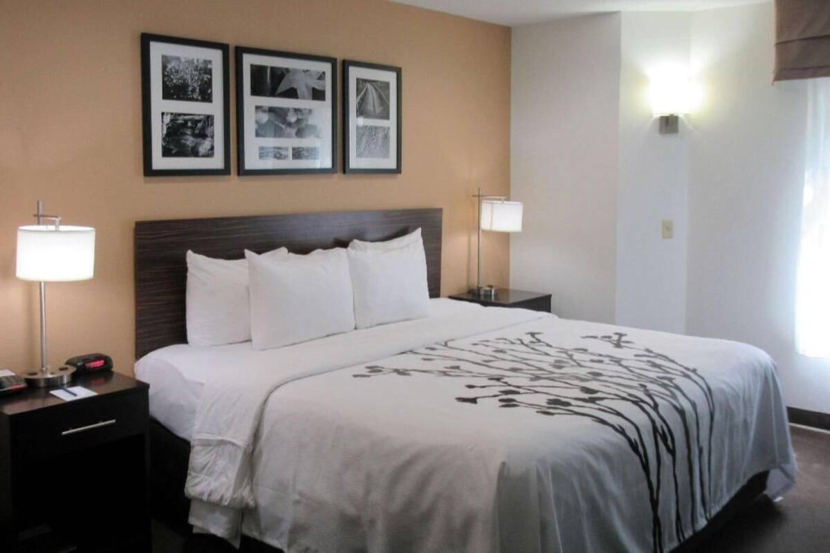 A hotel room with a large bed, two bedside tables, a nightstand, and wall-mounted lamps. There are three framed pictures on the wall above the bed.