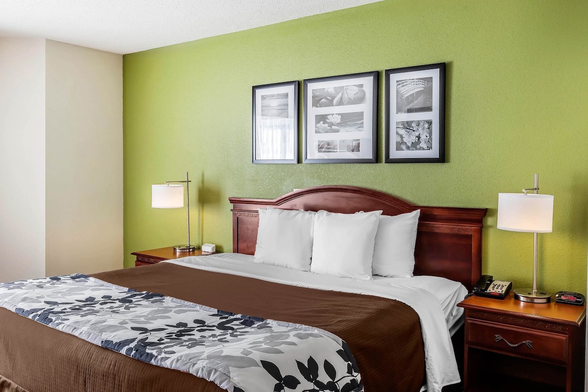 Quarto de hotel com uma cama grande, duas mesas de cabeceira com abajures, um painel de cabeceira de madeira e três quadros na parede.