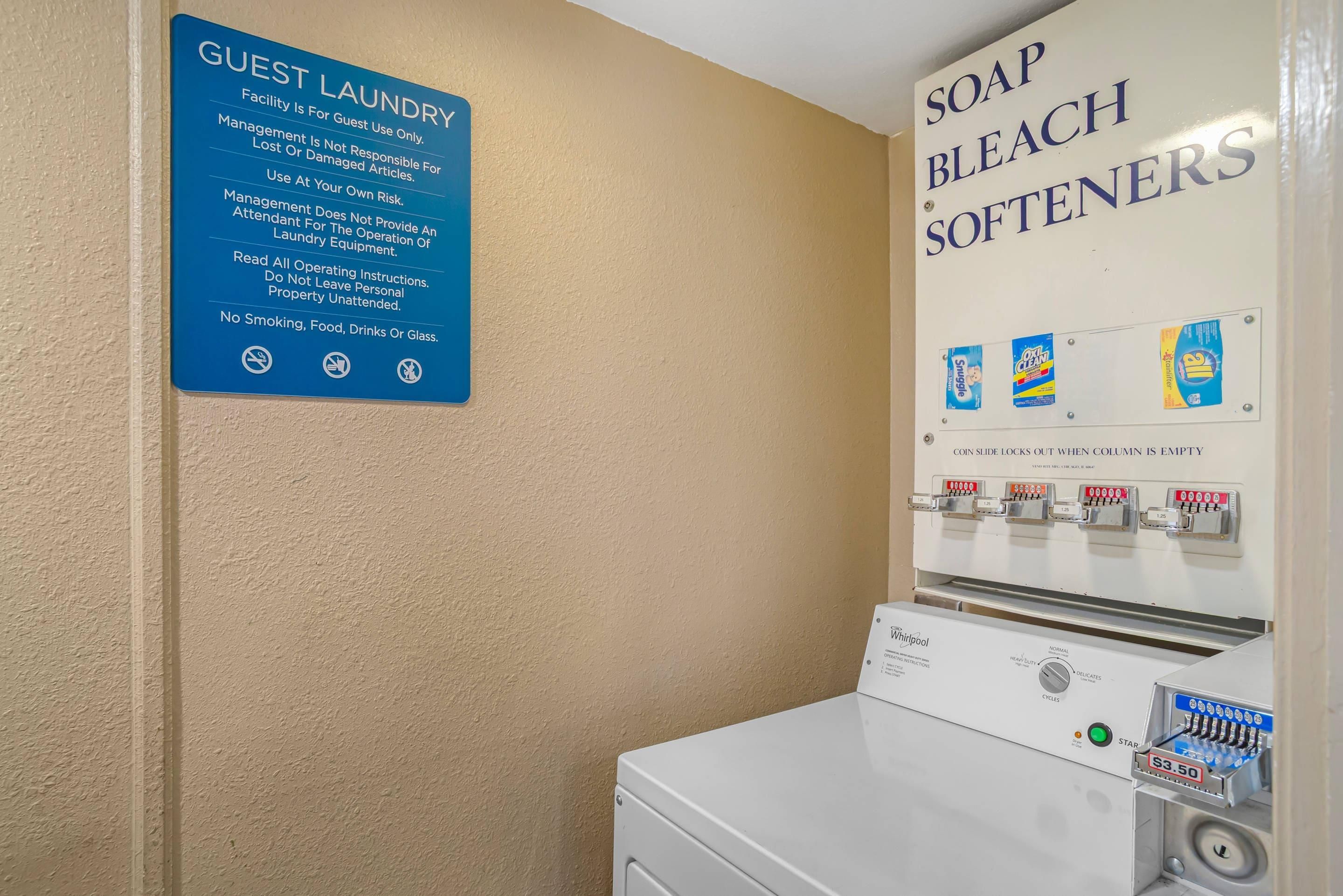 Een wasserette voor gasten, met een bord waarop de regels staan en een wanddispenser voor wasmiddel en bleekmiddel.'