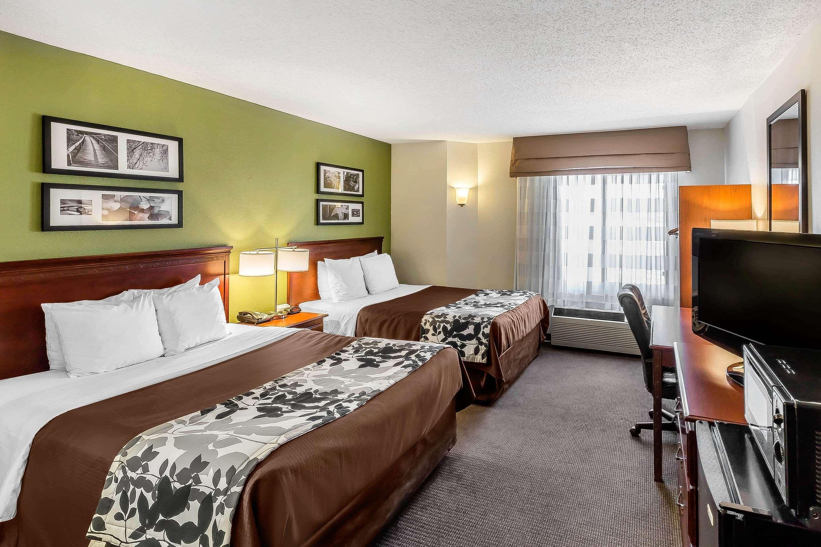 A hotel room with two beds, a desk with a TV, and a window with curtains.