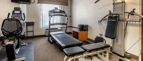A hotel room with a treadmill, stationary bike, rowing machine, and a TV mounted on the wall.