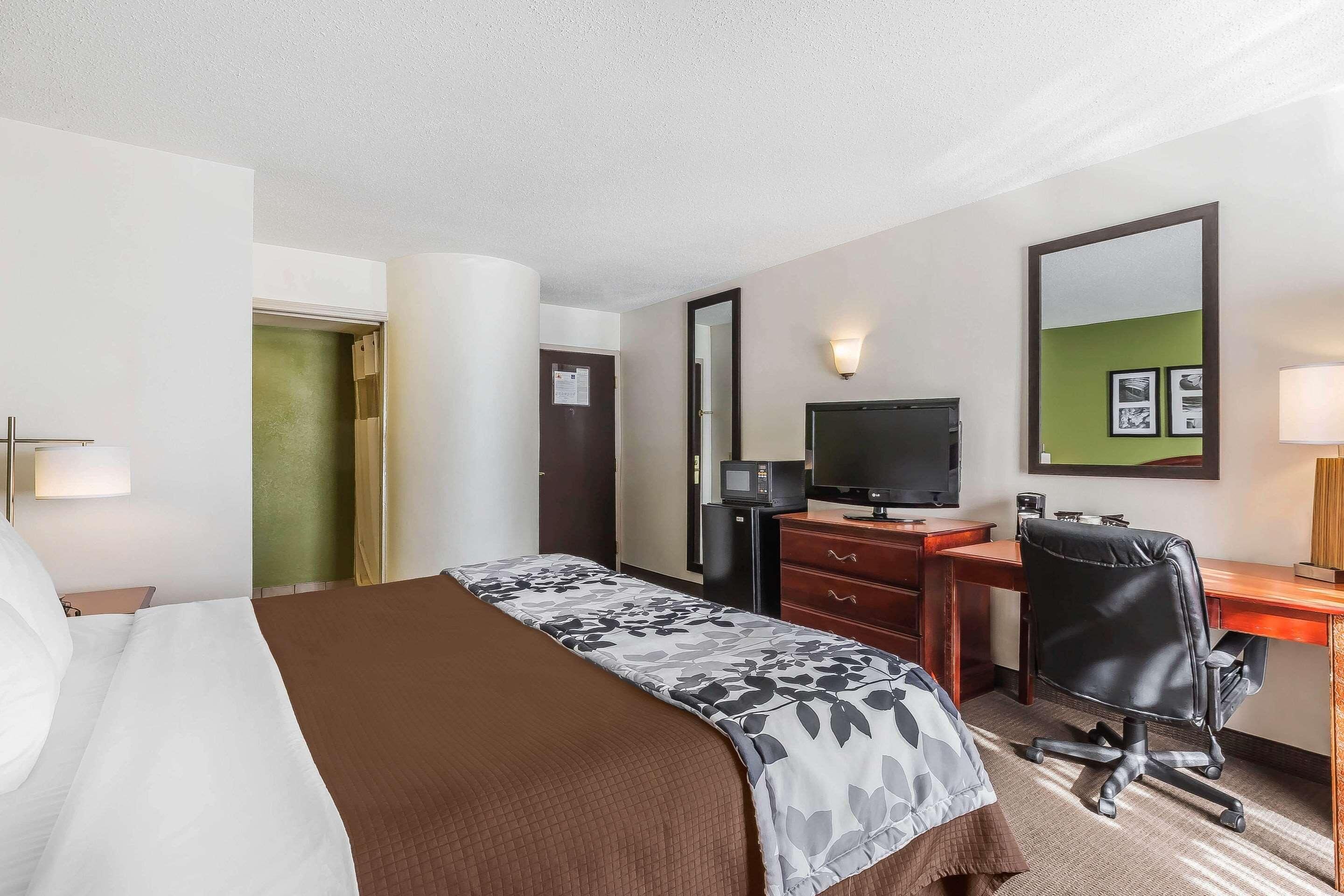 A hotel room with a bed, a desk, a chair, a TV, and a mirror.