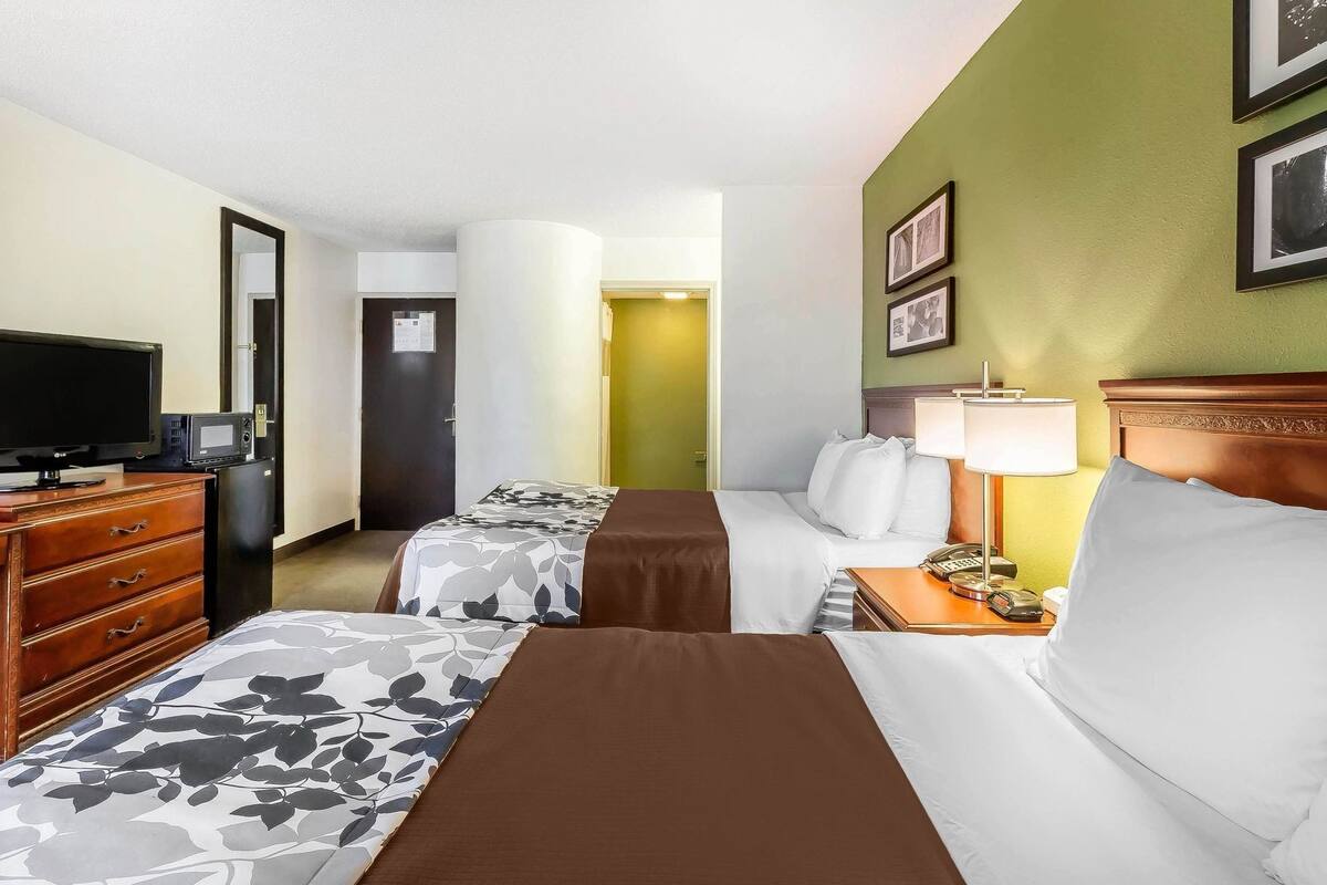 A hotel room with two beds, a TV, a desk with a lamp, and a dresser.