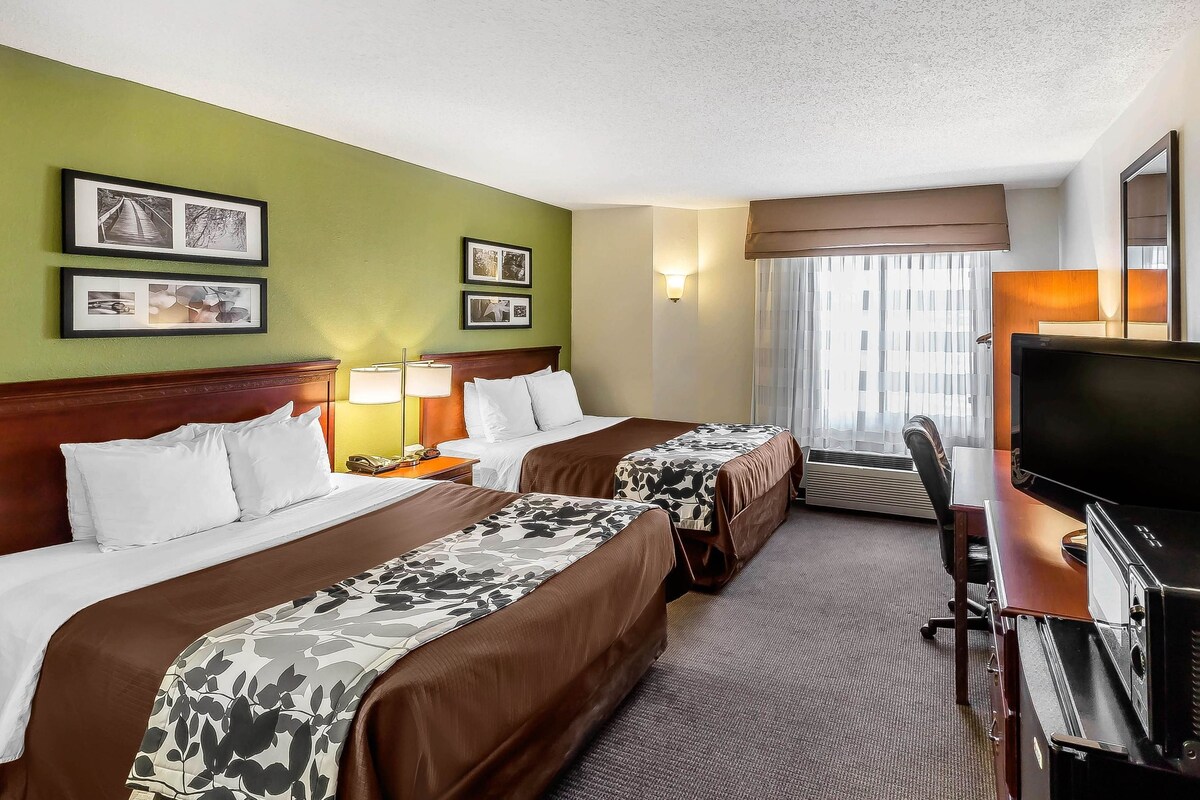 A hotel room with two beds, a desk with a TV, and a window with curtains.