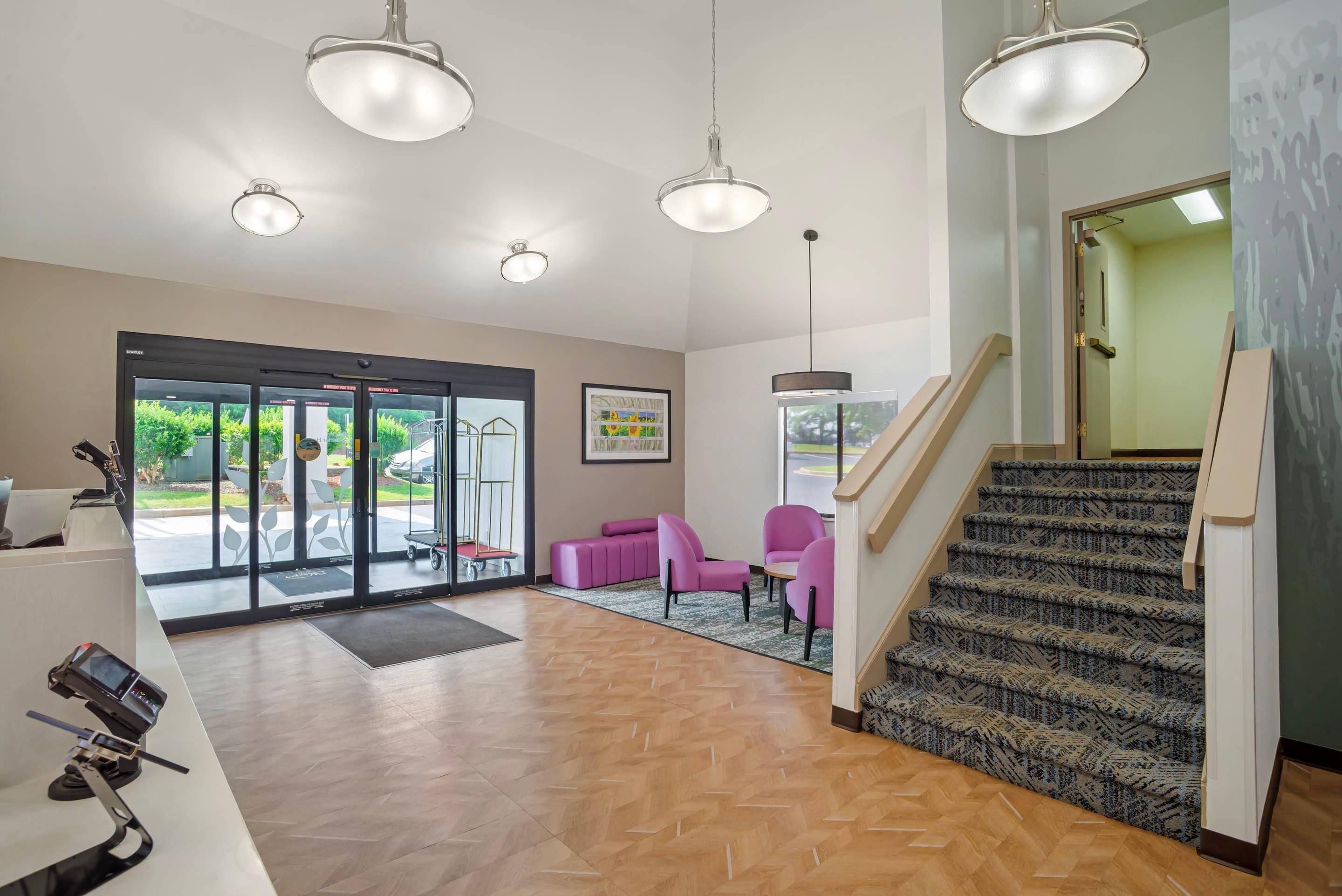 A hotel lobby with a reception desk, a staircase, and a seating area with chairs.