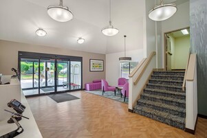 A hotel lobby with a reception desk, a staircase, and a seating area with chairs.