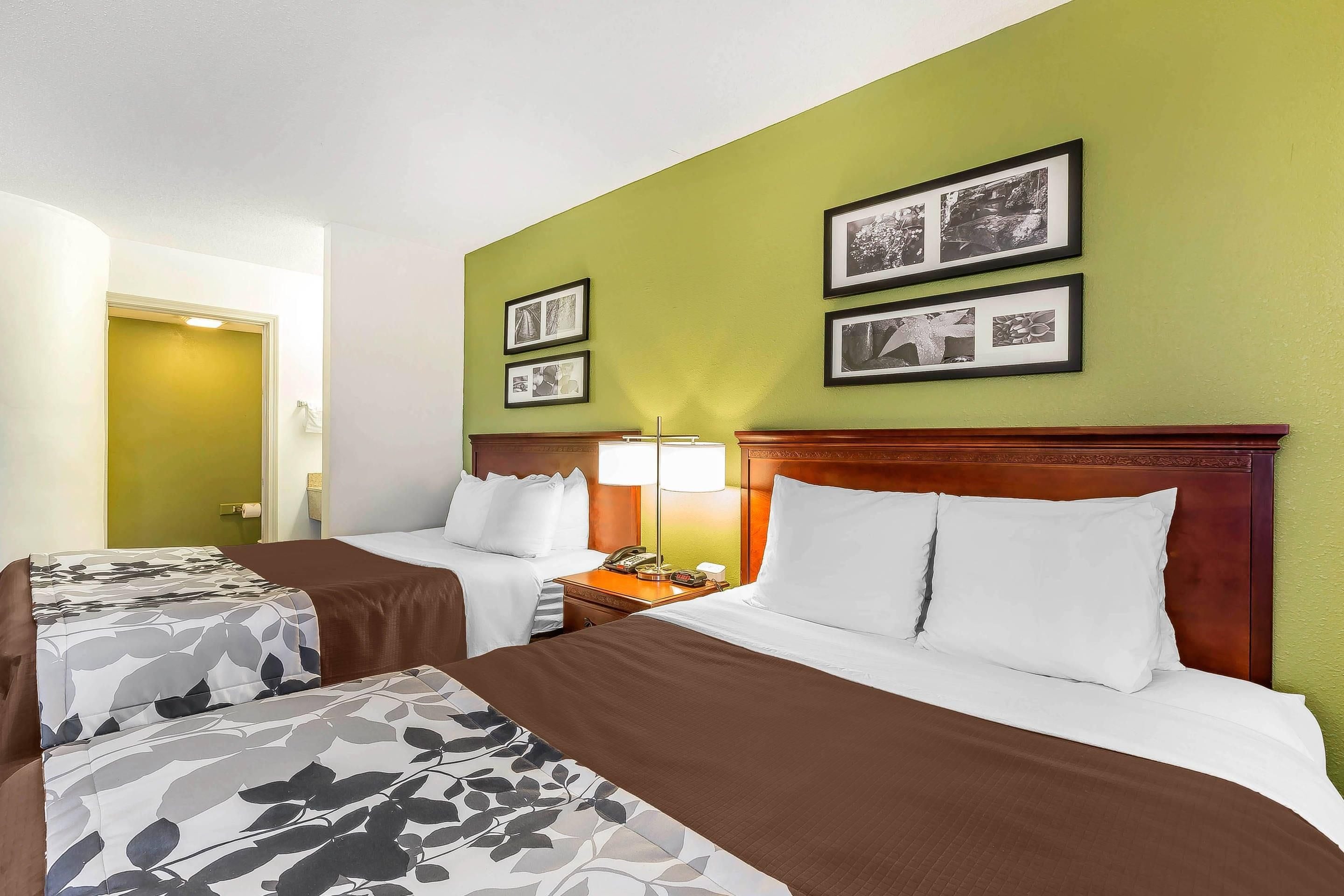 Habitación de hotel con dos camas, una mesita de noche con lámpara y cuadros en la pared.
