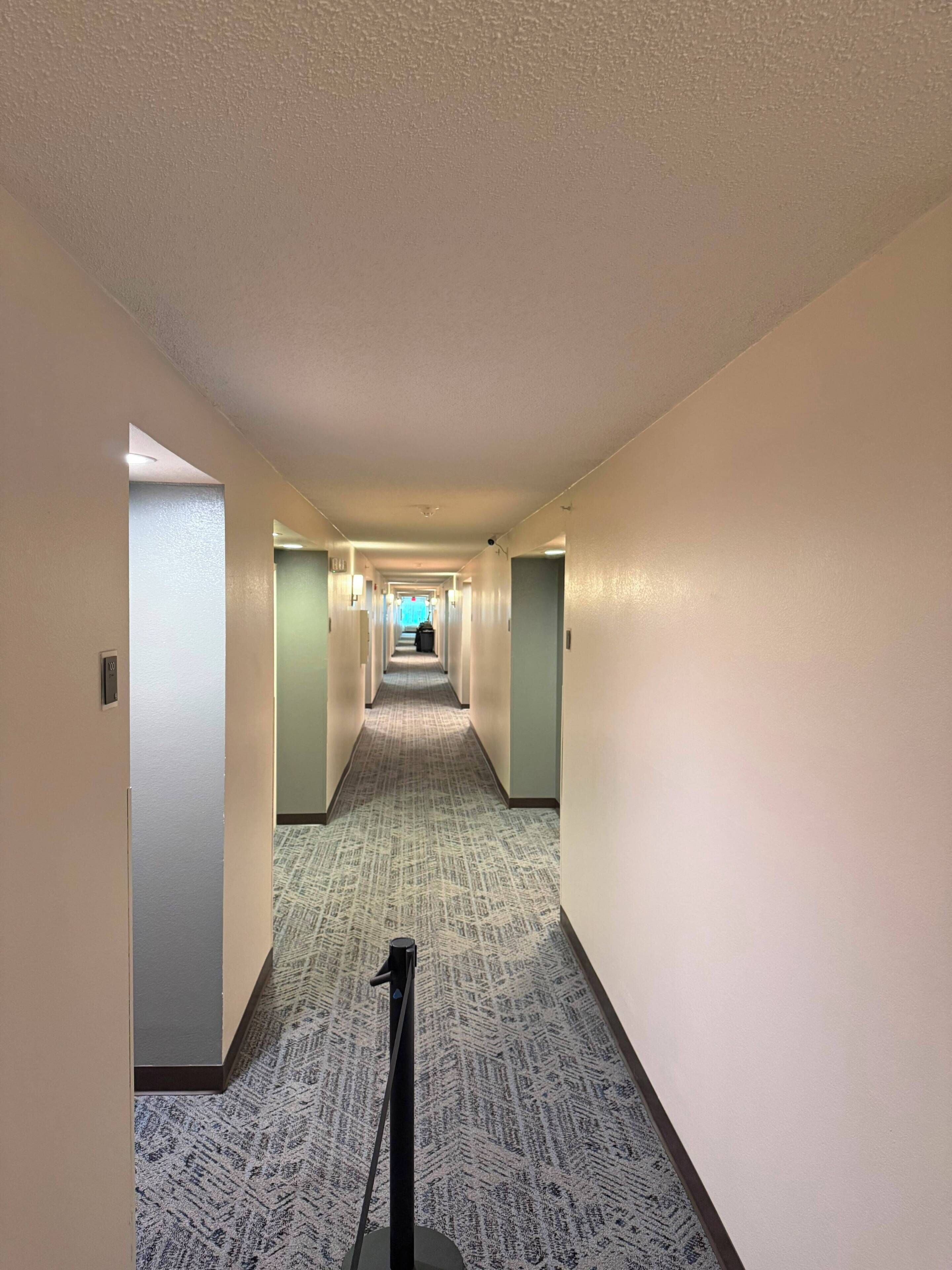 Un pasillo de hotel con piso alfombrado, puertas a ambos lados y una cámara de seguridad en el techo.