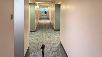 Un pasillo de hotel con piso alfombrado, puertas a ambos lados y una cámara de seguridad en el techo.