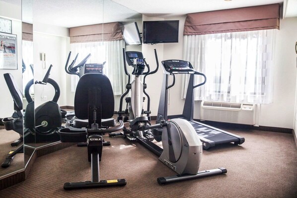 A hotel gym with cardio machines, weight equipment, and a TV on the wall.
