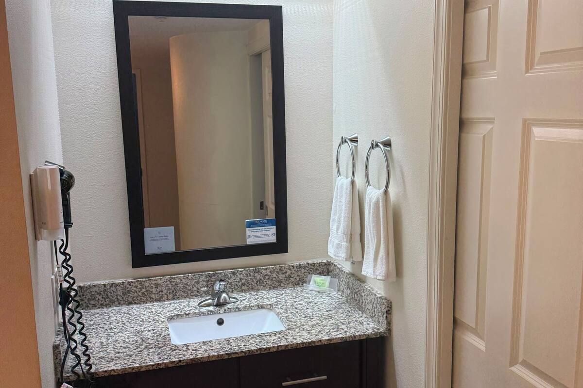 A bathroom with a granite countertop sink, a mirror, a towel rack, and a door.