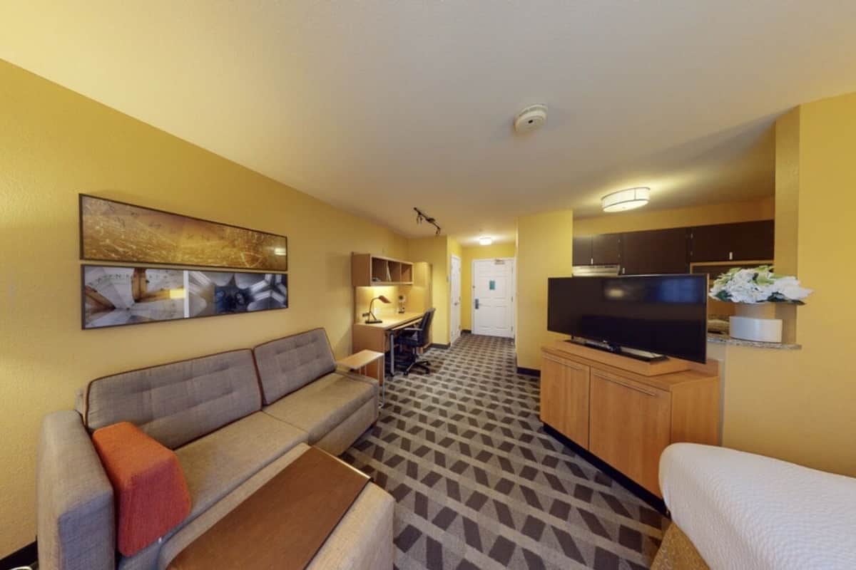 Una habitación de hotel compacta con sofá, una pequeña televisión, kitchenette y piso estampado.