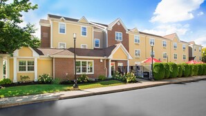 A multi-story hotel with a brick facade, a well-maintained lawn, and red umbrellas in the entrance area. - Residences at International Place (Tewksbury)