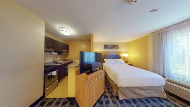 A hotel room with a kitchenette, a bed, a television, and a window with curtains. - Residences at International Place (Tewksbury)