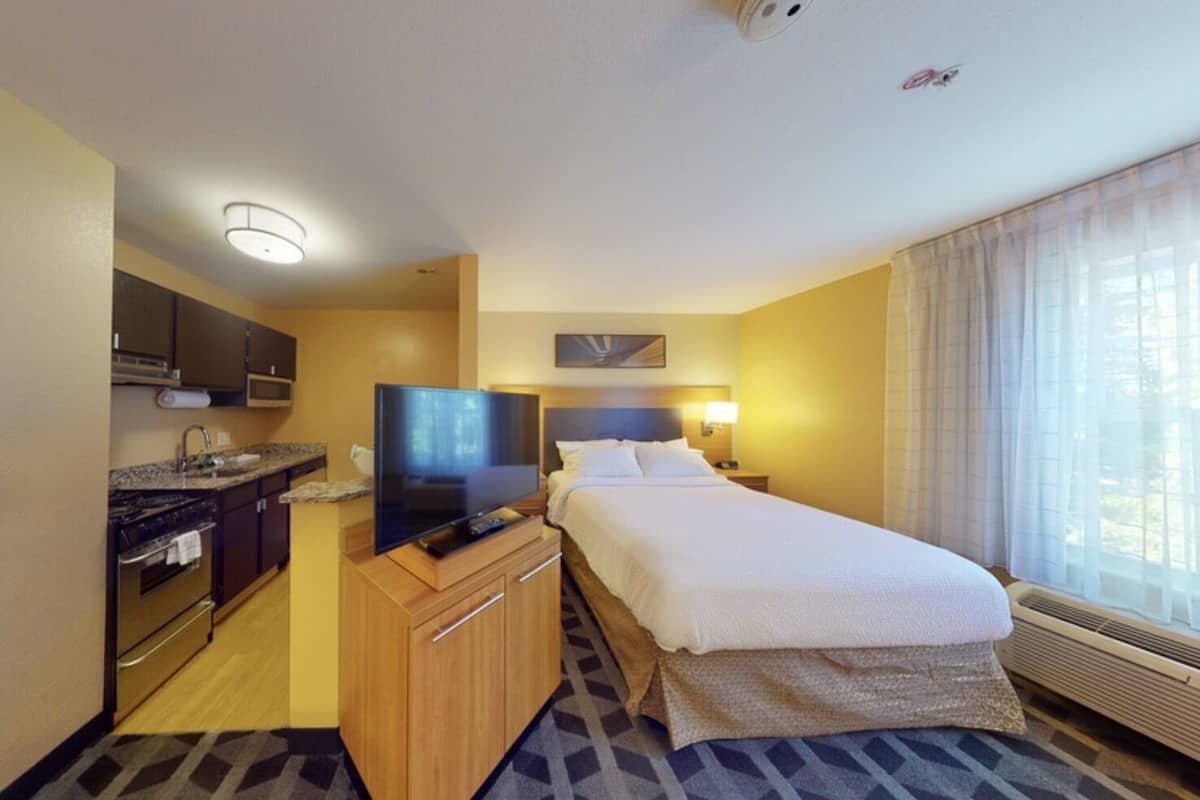Habitación de hotel con kitchenette, cama, televisor y ventana con cortinas.