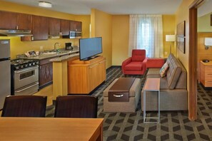 A compact hotel room with a kitchenette, a dining area, a sofa, and a TV. - Residences at International Place (Tewksbury)