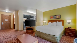 A hotel room with a bed, bedside tables, a television, a kitchenette, and a patterned carpet.