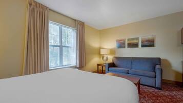 Ein Hotelzimmer mit Bett, Sofa, Lampe und einem fensterbepflanzten Fenster.
