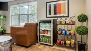 Une pièce comprenant un fauteuil en cuir, un réfrigérateur rempli de boissons, une étagère avec des en-cas et un tableau accroché au mur.