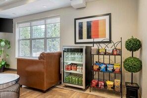 A room with a leather chair, a refrigerator stocked with beverages, a snack shelf, and a painting on the wall.