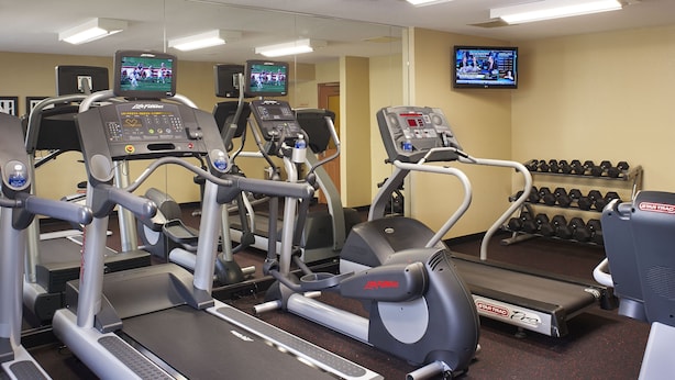A gym with treadmills, elliptical machines, and a television displaying a sports event.