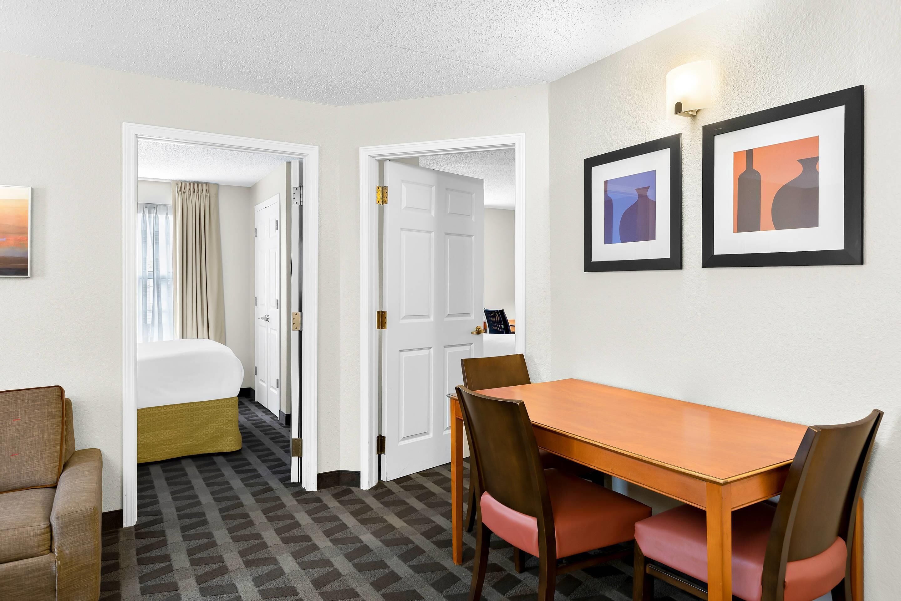 Una habitación de hotel con una cama, una mesa de comedor con sillas y un pasillo que conduce a otra habitación.