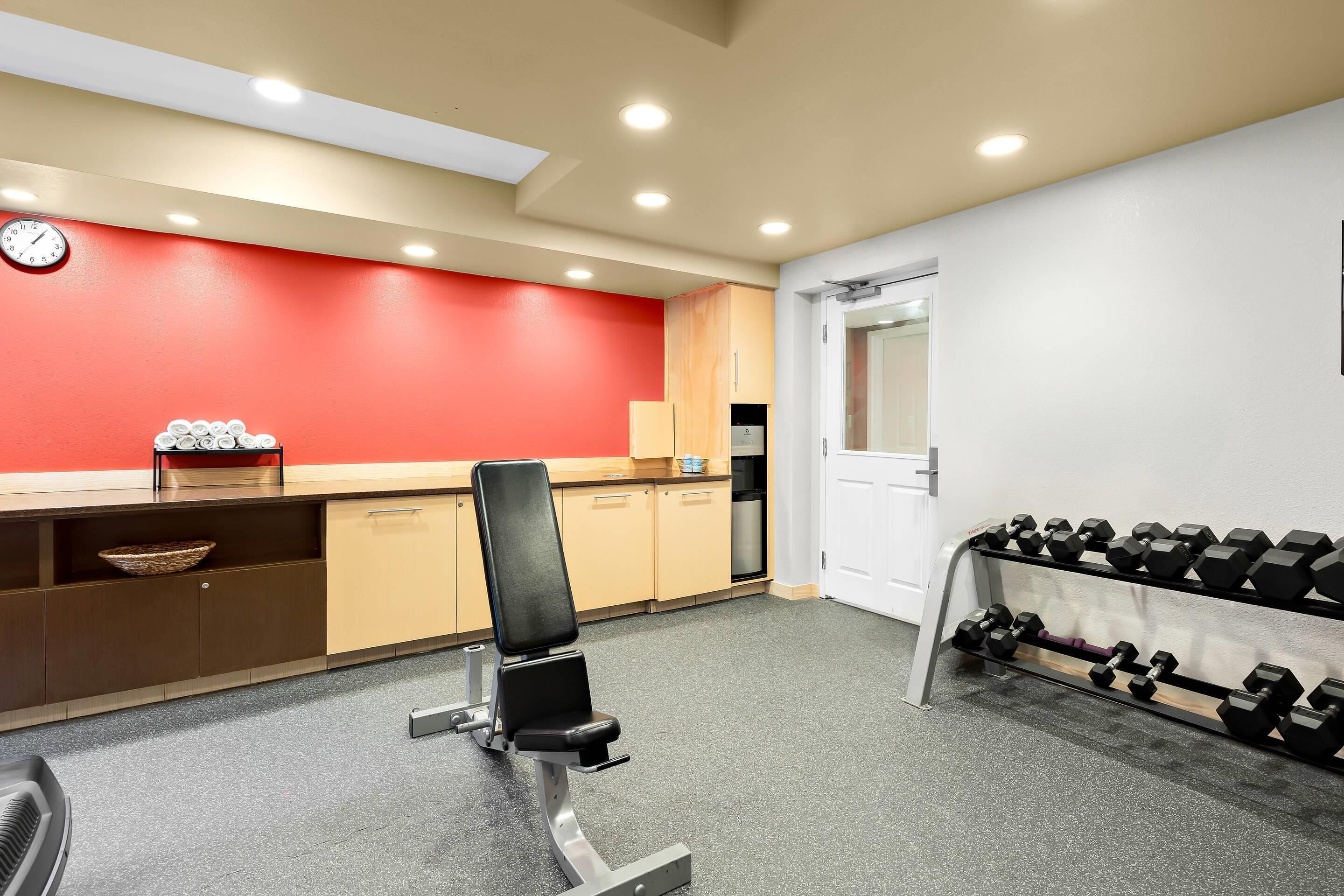 A gym with exercise equipment, a dumbbell rack, and a red wall.