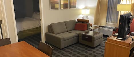 A hotel room with a sofa, a desk with a computer, a lamp, and a bed.