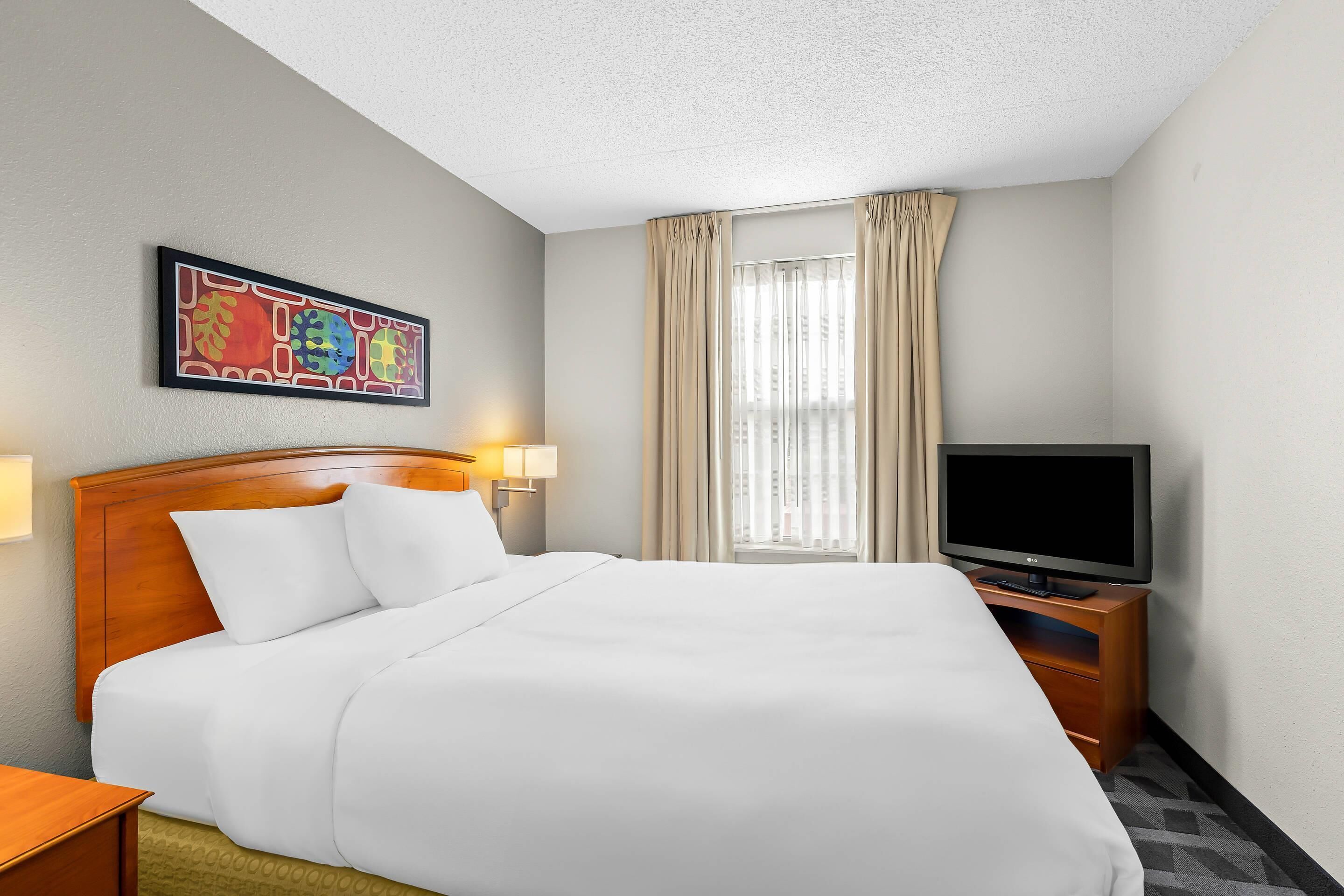 A hotel room with a neatly made bed, a television on a wooden stand, and a painting on the wall.