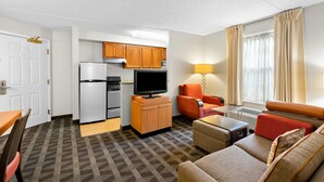 A compact hotel room with a kitchenette, a sofa, a dining table, and a TV.