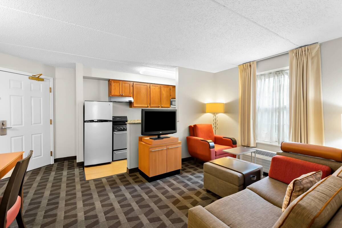 Une chambre d’hôtel compacte comprenant un coin cuisine, un canapé, une table à manger et un téléviseur.