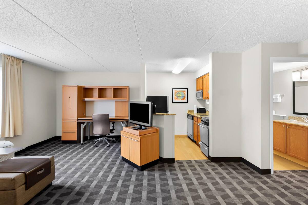 Une chambre d’hôtel compacte comprenant un coin cuisine, un bureau avec un ordinateur, une télévision et un lit.