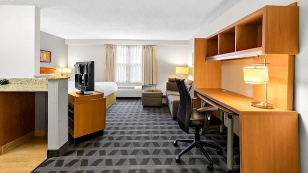 A hotel room with a bed, desk, chair, television, and a small kitchenette.