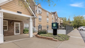 A residential building with a 'WELCOME' sign, a brick facade, and a paved sidewalk.