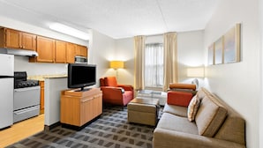 A compact hotel room with a kitchenette, a sofa, a small table, and a TV.