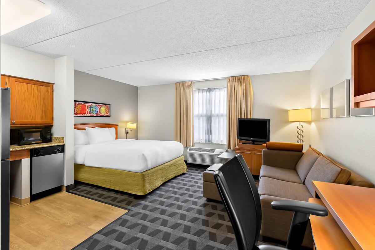 Une chambre d’hôtel équipée d’un lit, d’un bureau avec un micro-ondes, d’une télévision, d’un canapé et d’une chaise.