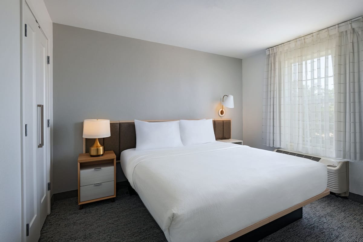 Een hotelkamer met een groot bed, nachtkastjes, een lamp, een verwarming en een raam met gordijnen.