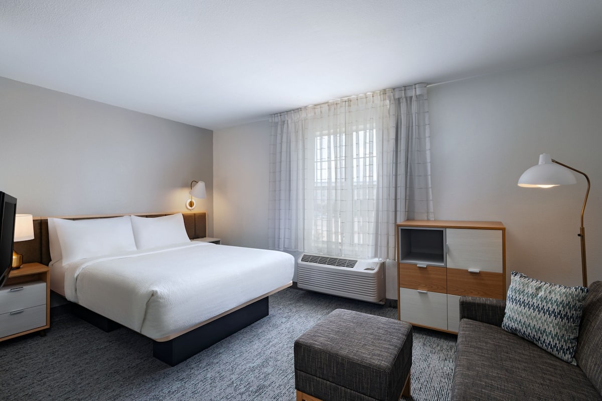 Een hotelkamer met een groot bed, een bureau met een lamp, een bank en een raam met gordijnen.