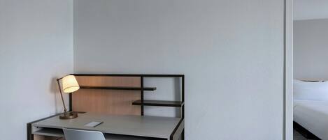 A hotel room with a desk, chair, lamp, and a bed.